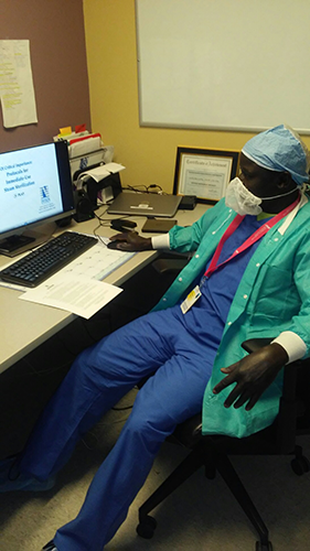 Bechak Deng in scrubs working at his workplace desk